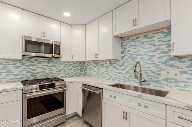 kitchen with a sink, light stone counters, tasteful backsplash, stainless steel appliances, and white cabinets