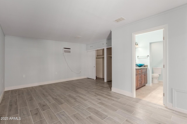 unfurnished bedroom featuring a wall mounted air conditioner, visible vents, a closet, connected bathroom, and light wood finished floors