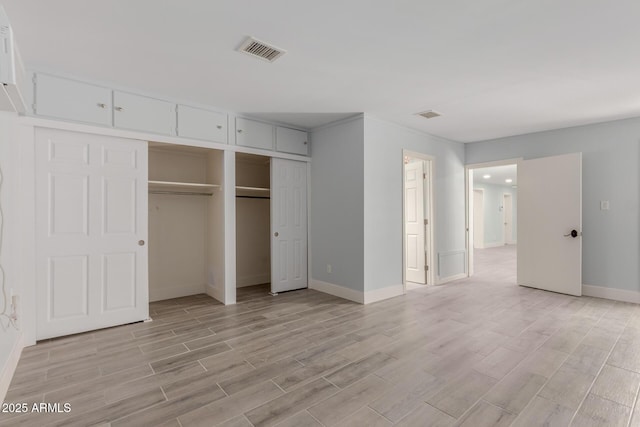 unfurnished bedroom featuring multiple closets, baseboards, visible vents, and wood tiled floor