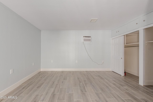 unfurnished bedroom with baseboards, a wall mounted AC, and wood finish floors