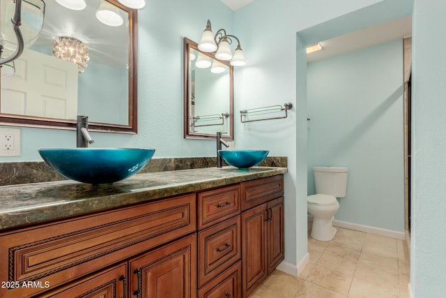 bathroom with double vanity, toilet, baseboards, and a sink