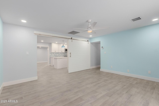 unfurnished living room with light wood-style floors, a barn door, a ceiling fan, and visible vents