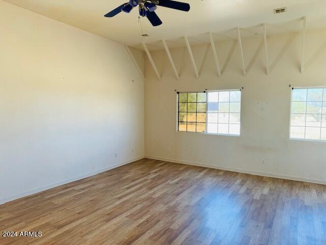 unfurnished room with ceiling fan, wood-type flooring, and vaulted ceiling with beams