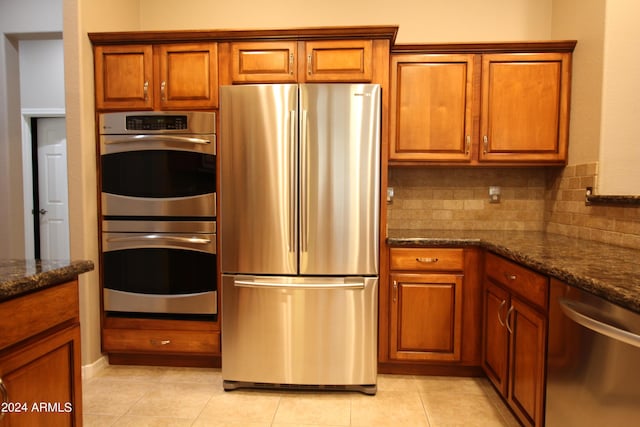 kitchen featuring appliances with stainless steel finishes, backsplash, light tile patterned floors, and dark stone counters