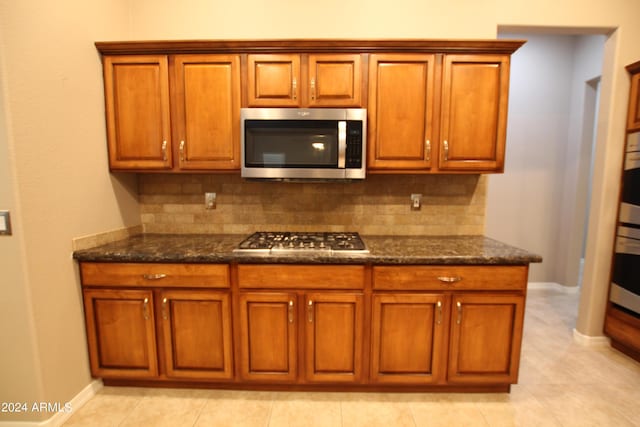 kitchen featuring decorative backsplash, appliances with stainless steel finishes, light tile patterned floors, and dark stone countertops