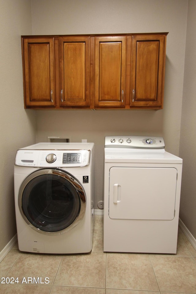 clothes washing area with washer and clothes dryer, cabinets, and light tile patterned floors