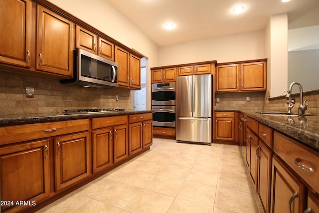 kitchen with sink, stainless steel appliances, backsplash, dark stone counters, and light tile patterned flooring