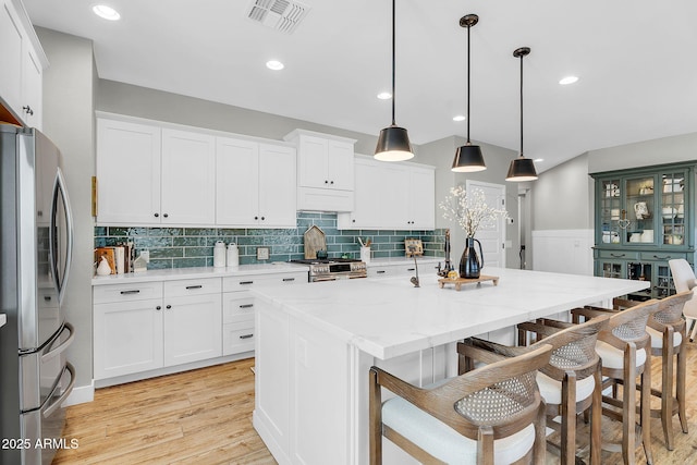 1335 W Via Del Oro, San Tan Valley, AZ 85140 - kitchen with stainless steel appliances, light wood finished floors, a kitchen bar, tasteful backsplash, and white cabinetry