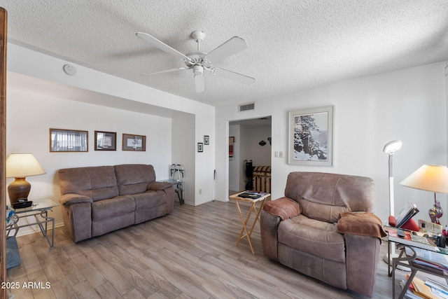 living room with a textured ceiling, light wood-style flooring, visible vents, and a ceiling fan