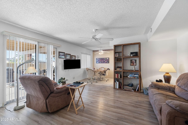 living area featuring light wood-style floors, ceiling fan, and a textured ceiling