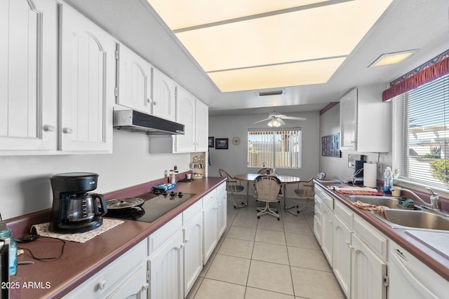 kitchen with dark countertops, under cabinet range hood, white cabinets, and a sink