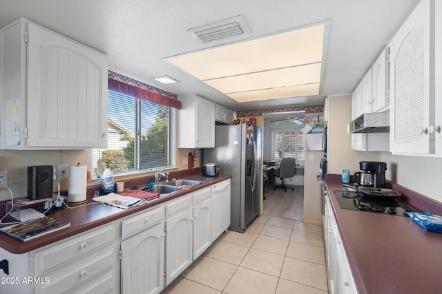 kitchen with light tile patterned floors, dark countertops, white cabinetry, a sink, and under cabinet range hood