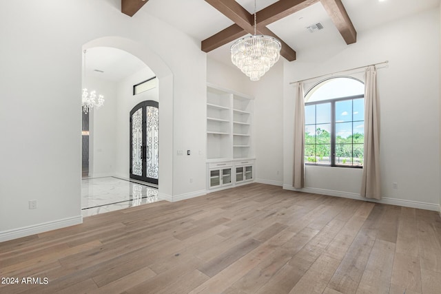 unfurnished living room featuring beam ceiling, french doors, coffered ceiling, an inviting chandelier, and light hardwood / wood-style floors