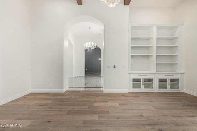 unfurnished living room featuring built in features, a chandelier, and hardwood / wood-style flooring