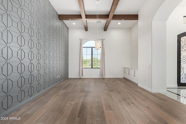 empty room with beam ceiling, a notable chandelier, coffered ceiling, and light wood-type flooring