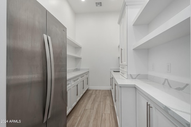 kitchen with white cabinets, stainless steel fridge, and light stone counters