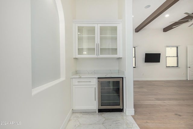 bar featuring white cabinets, wine cooler, ceiling fan, light stone countertops, and beam ceiling