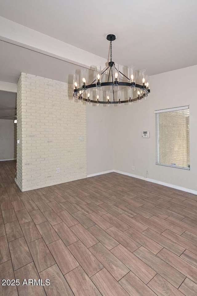 spare room featuring an inviting chandelier, baseboards, brick wall, and wood finish floors