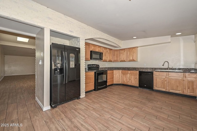 kitchen featuring wood finish floors, black appliances, a sink, recessed lighting, and dark stone counters