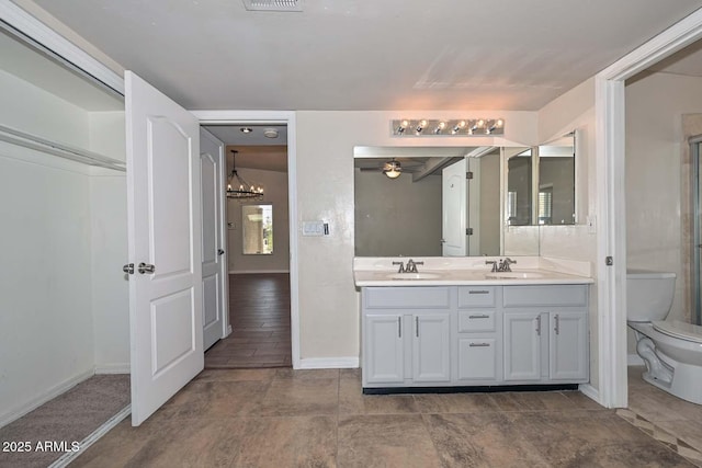 full bath featuring double vanity, ceiling fan with notable chandelier, toilet, and a sink