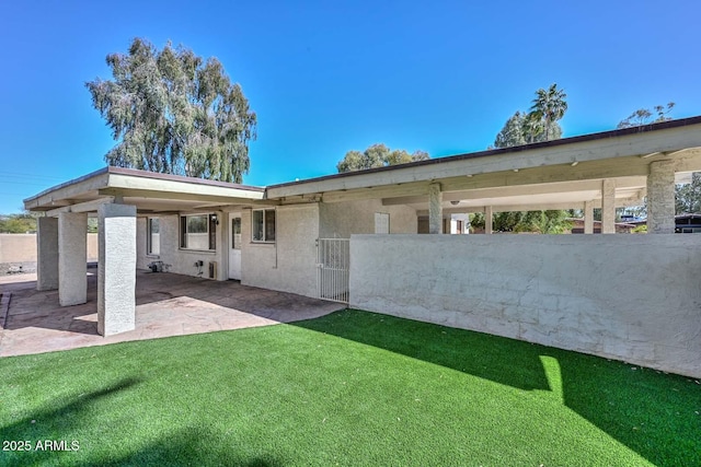 rear view of house featuring stucco siding, a gate, fence, a yard, and a patio area