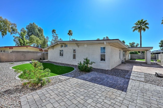 rear view of house featuring an attached carport, fence, stucco siding, a lawn, and driveway