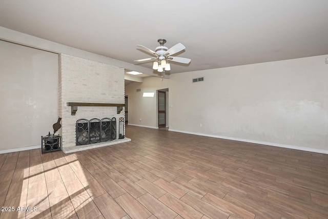 unfurnished living room with wood finished floors, visible vents, lofted ceiling, ceiling fan, and a brick fireplace