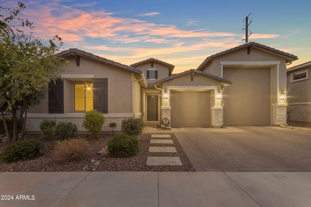 view of front of property featuring a tiled roof, stucco siding, a garage, stone siding, and driveway