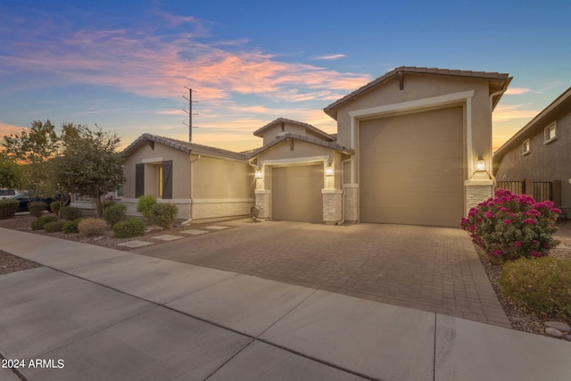 view of front facade with decorative driveway, stone siding, an attached garage, and stucco siding