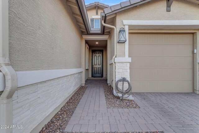 property entrance with a tile roof, decorative driveway, a garage, and stucco siding