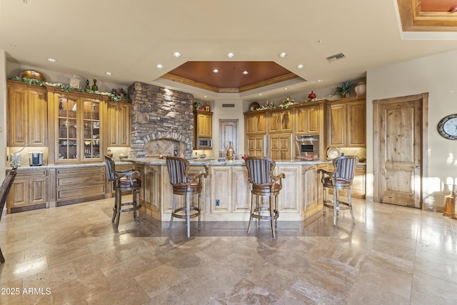 13249 E Summit Dr, Scottsdale, AZ 85259 - kitchen featuring a raised ceiling, brown cabinets, appliances with stainless steel finishes, a breakfast bar area, and light stone countertops