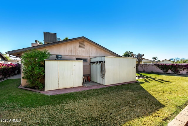 rear view of property with a lawn, central AC unit, and a shed