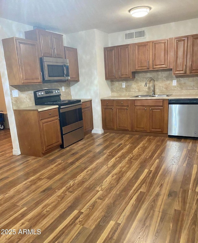 kitchen featuring dark wood-type flooring, appliances with stainless steel finishes, backsplash, and sink