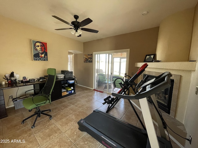 exercise room featuring light tile patterned floors, a tile fireplace, and ceiling fan