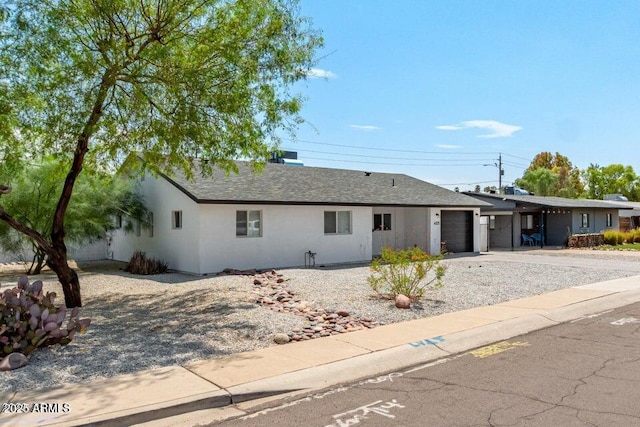 ranch-style home with stucco siding, an attached garage, roof with shingles, and driveway