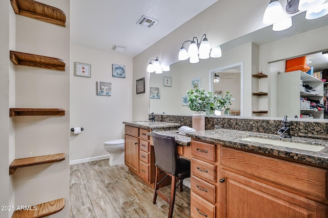 7125 W Canterbury Dr, Peoria, AZ 85345 - bathroom featuring wood finished floors, toilet, double vanity, ceiling fan, and baseboards