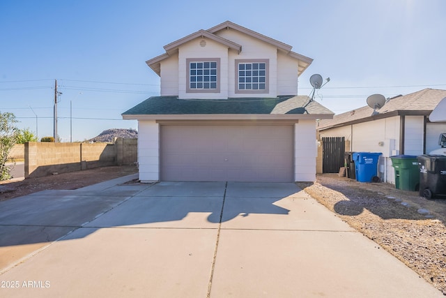 traditional-style house featuring an attached garage, a shingled roof, driveway, and fence