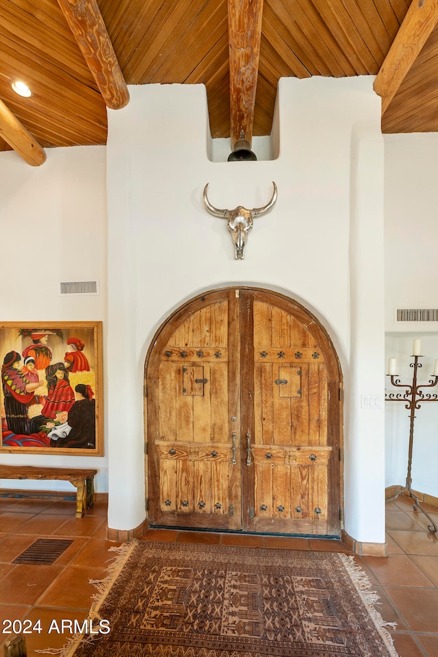 entryway with beamed ceiling, a towering ceiling, wooden ceiling, and dark tile patterned flooring