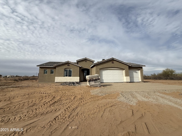 mediterranean / spanish-style house featuring stucco siding, an attached garage, a tile roof, and dirt driveway