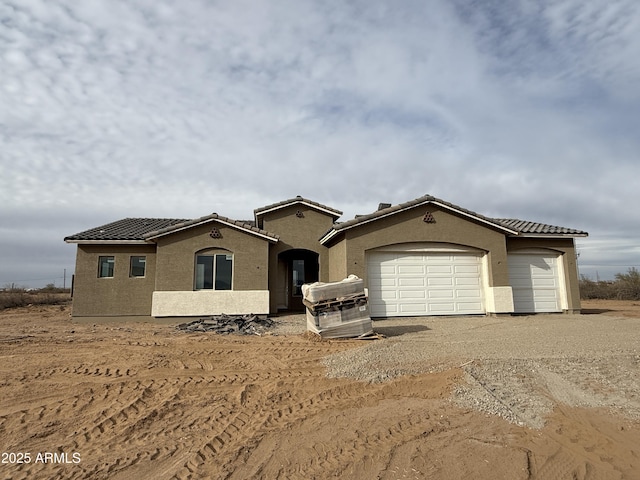 mediterranean / spanish-style house with a tile roof, an attached garage, driveway, and stucco siding