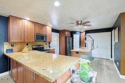 kitchen with ceiling fan, light stone countertops, kitchen peninsula, decorative backsplash, and appliances with stainless steel finishes