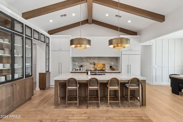 kitchen featuring a large island with sink, paneled refrigerator, light stone counters, and pendant lighting