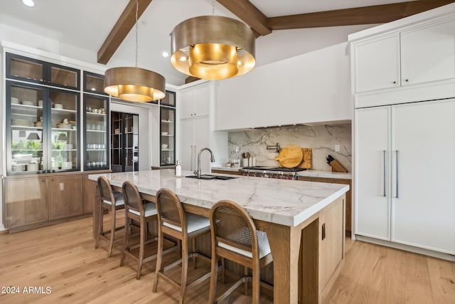 kitchen featuring an island with sink, light stone counters, sink, white cabinetry, and tasteful backsplash