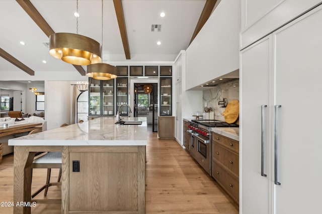 kitchen featuring light stone counters, range with two ovens, an island with sink, white cabinets, and sink