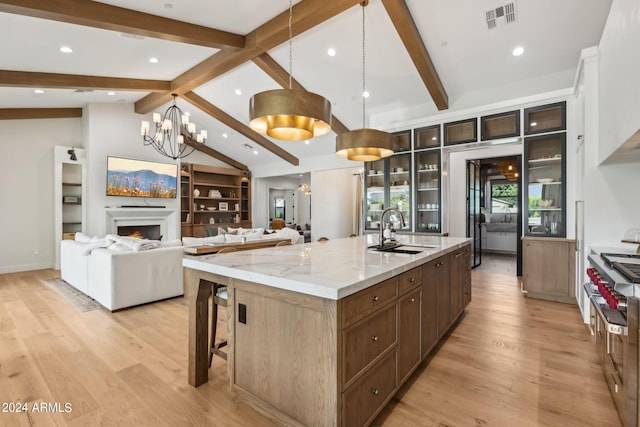 kitchen with sink, a large island, vaulted ceiling with beams, light stone counters, and stainless steel range