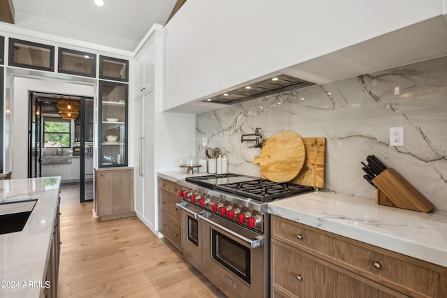 kitchen featuring double oven range, light wood-type flooring, light stone counters, and tasteful backsplash