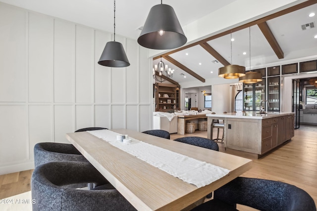 dining room with sink, lofted ceiling with beams, and light wood-type flooring