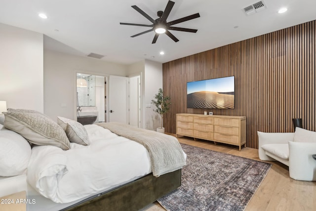 bedroom with ceiling fan, light wood-type flooring, ensuite bathroom, and wooden walls