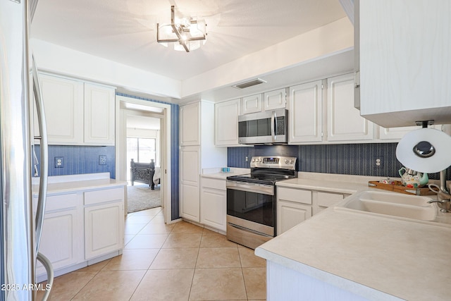 kitchen featuring sink, light tile patterned floors, stainless steel appliances, and white cabinets