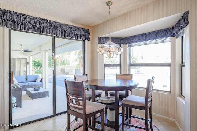 tiled dining room featuring ceiling fan with notable chandelier and a textured ceiling